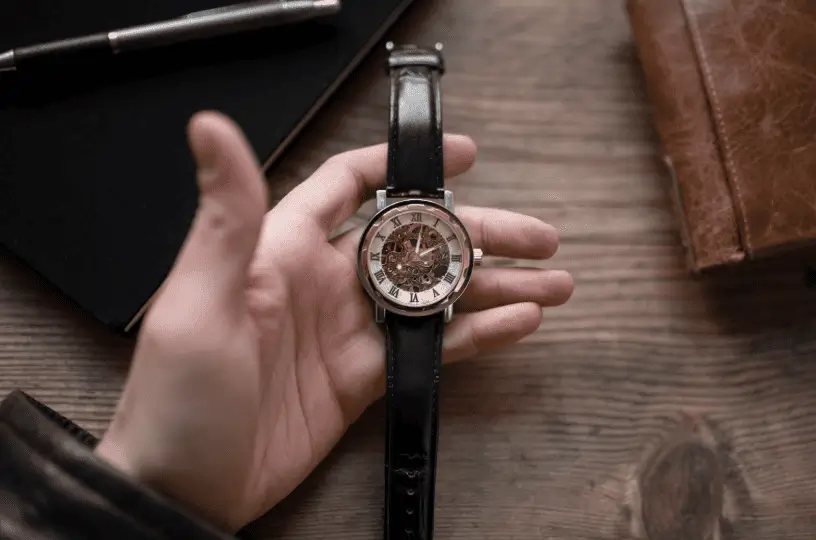 A skeleton mechanical watch with a black leather strap displayed on a hand over a wooden surface.