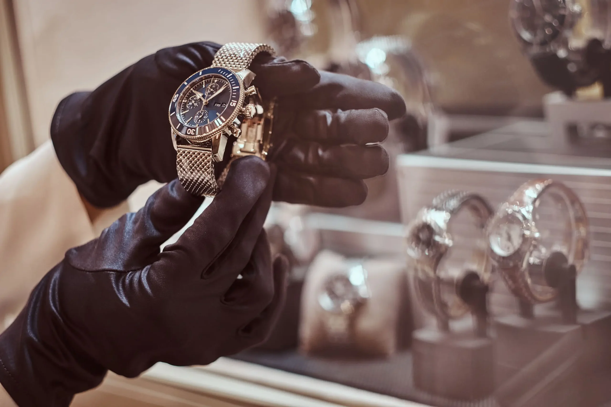 Gloved hands holding a luxury men's watch inside a high-end jewelry store display.