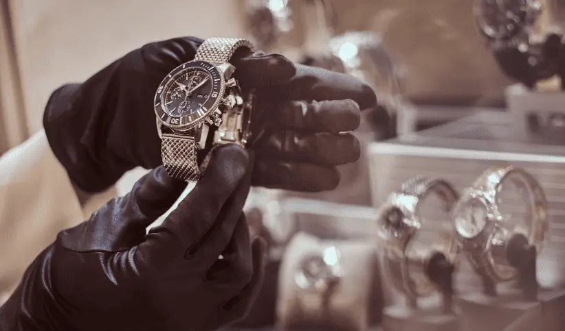 Gloved hands holding a steel chronograph watch inside a watch boutique.