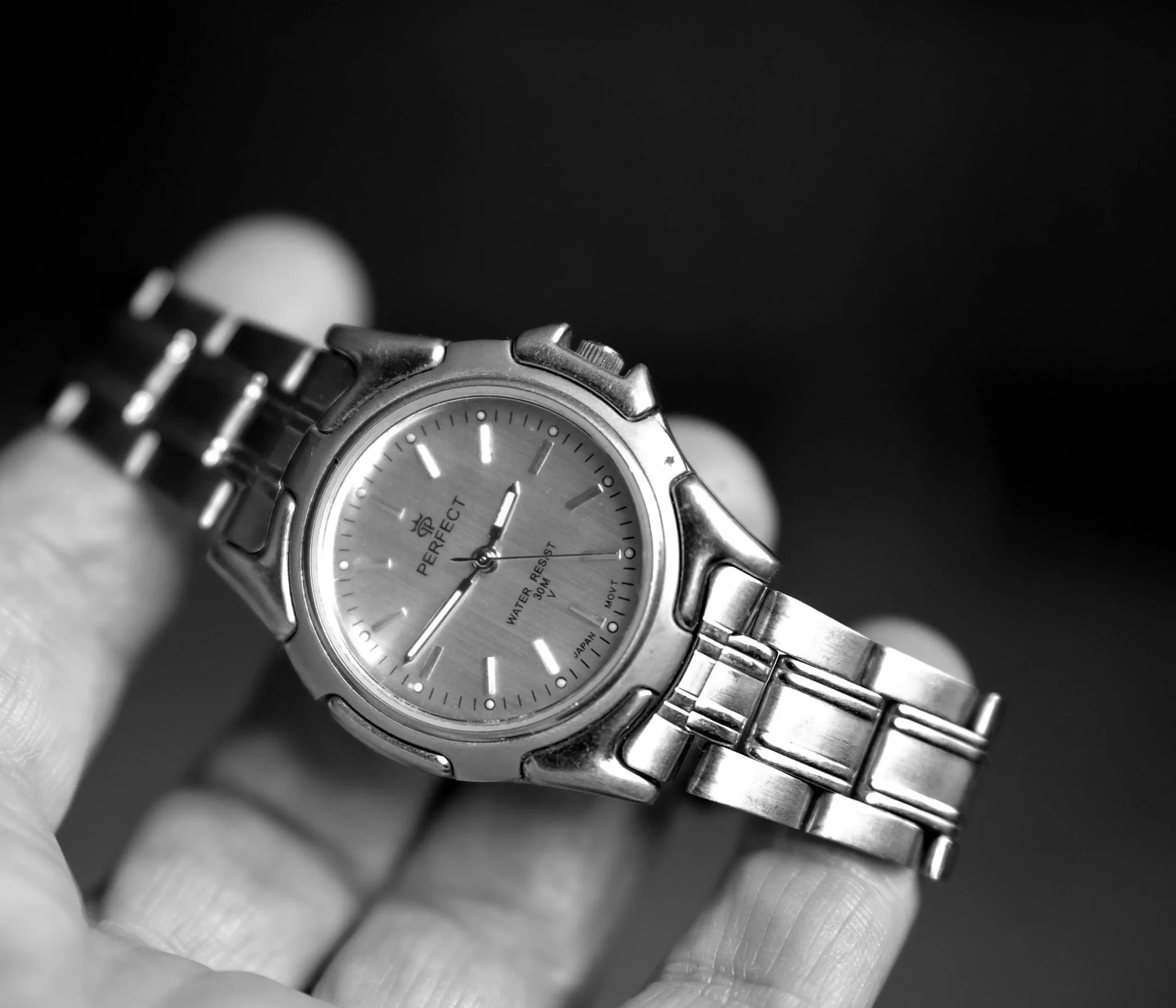 A close-up shot of a person's hand holding a vintage-style silver "Perfect" watch, emphasizing the simplicity and elegance of the watch design.